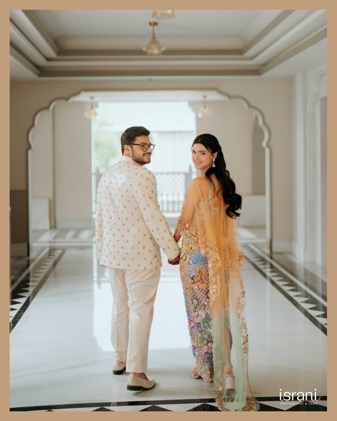 Beautiful newly married Indian couple walking under a heritage palace archway with petals falling